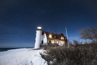 Lighthouse amidst buildings against sky at night