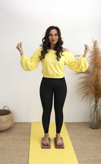 Portrait of young woman with arms raised standing against wall