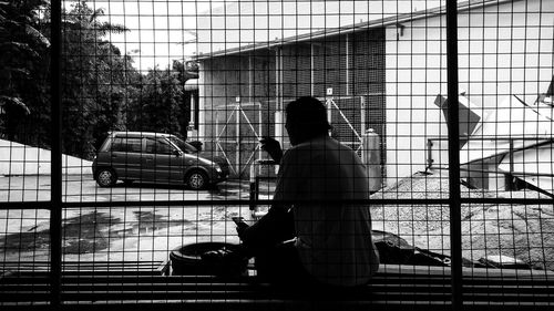 Rear view of man sitting on window sill against house