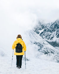 Back view of anonymous hiker with trekking poles walking on snowy ground in pyrenees mountains in andorra