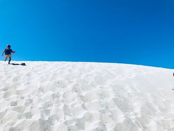 Man on snow covered land against clear blue sky