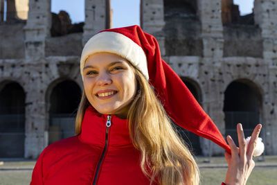 Beautiful blonde woman posing in front of the colosseum with santa claus hat.