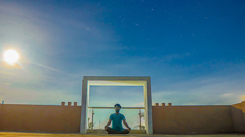 Rear view of woman sitting against building against sky