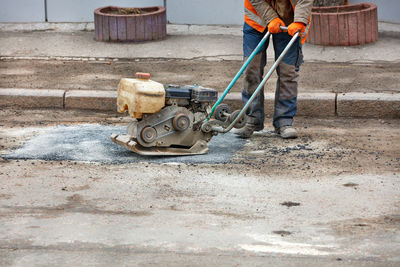 A worker rams fresh asphalt on a hole in an old road with a petrrol plate compactor.