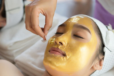 Cropped hand of massage therapist applying facial mask on young woman face in spa