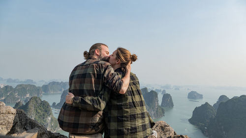 Couple kissing on mountain against clear sky
