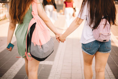 Back view of lesbian couple holding hands while walking in city