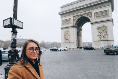 Portrait of young woman smiling while standing against arc de triomphe