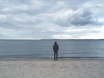 Man standing on beach against cloudy sky