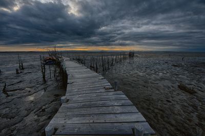 Wooden pier on beach against sky during sunset