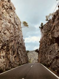 Empty road amidst rocks against sky
