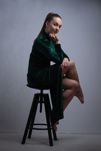 Young woman sitting on seat against wall