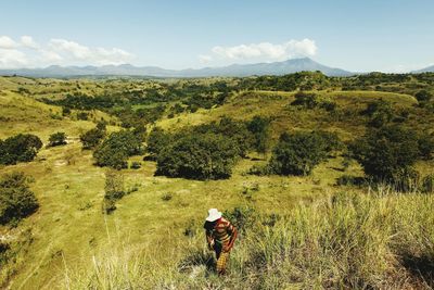 Man walking on grassy hill against sky