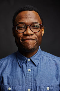 Close-up portrait of smiling man wearing eyeglasses against black background