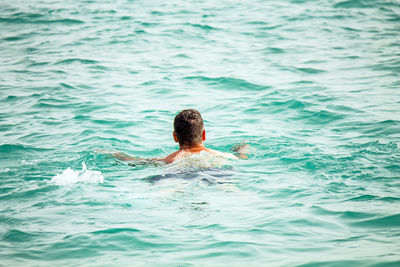 Rear view of mid adult man swimming in sea