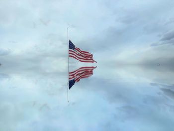 American flag reflecting on lake against cloudy sky