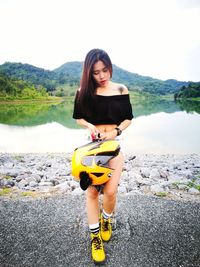 Woman holding helmet by lake