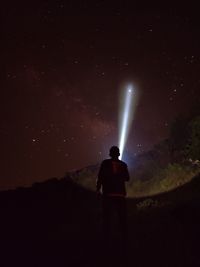 Rear view of silhouette hiker with flashlight watching stars during night