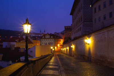 Illuminated street amidst buildings against sky at night