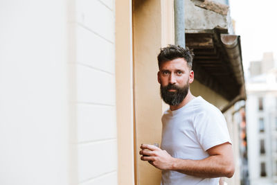 Bearded guy with hot drink resting on balcony