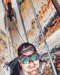 High angle portrait of young man wearing sunglasses with dog walking on footbridge