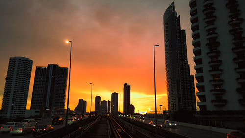 Cars on road by buildings against sky during sunset