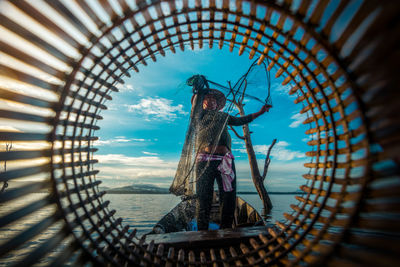 Fisherman holding fishing net seen through wicker basket