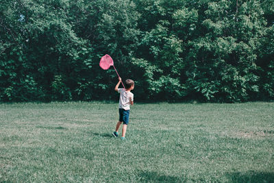 Rear view of boy holding net while standing on grassy land in park