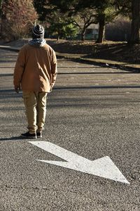 Rear view of man standing opposite to arrow sign on road 