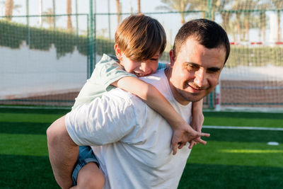 Happy father carrying son on back at sports ground