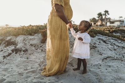 Side view of young toddler girl with mother’s pregnant belly