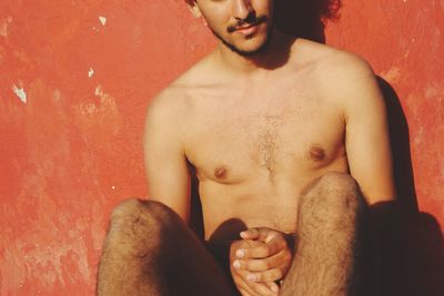 Midsection of shirtless man sitting against wall