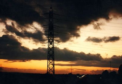 Silhouette of electricity pylon against cloudy sky