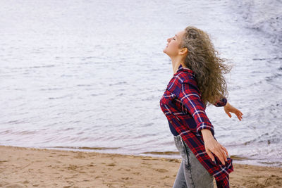  girl stands with her arms spread out to the sides against the background of the sea.