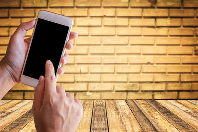 Midsection of person using mobile phone against brick wall