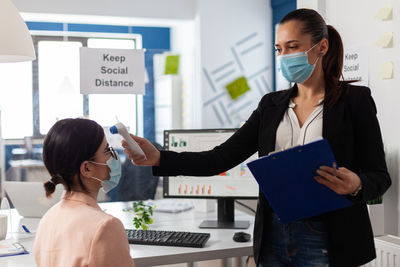 Businesswoman checking temperature of colleague