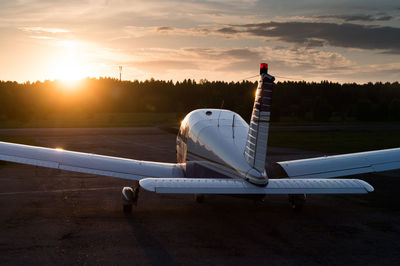 Airplane on airport runway against sky during sunset