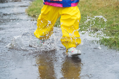 Low section of girl running through puddle