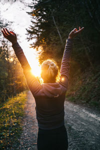 Rear view of woman with arms raised standing on road in forest