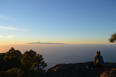 Man standing on rock against sky during sunset