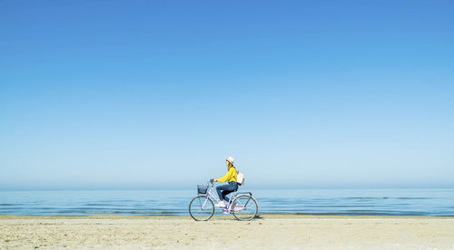 Man riding bicycle on beach against clear sky