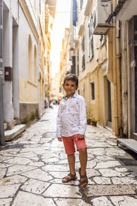 Full length portrait of boy standing on footpath amidst buildings