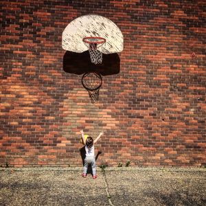 Small child playing basketball in front of brick wall