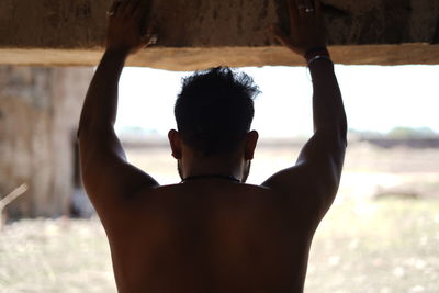 Rear view of shirtless man with arms raised