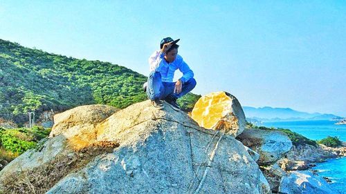 Man standing on rock by sea against mountain