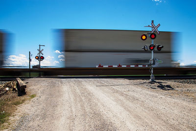 Crossing signal by railroad tracks against sky