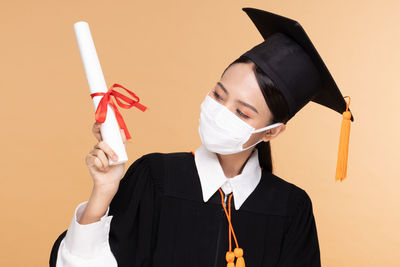 Portrait of young woman holding umbrella against gray background