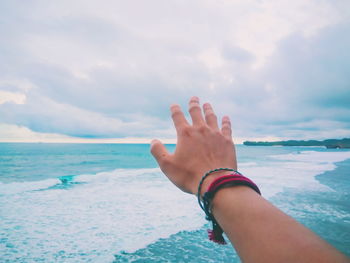 Cropped hand of person gesturing over sea against sky