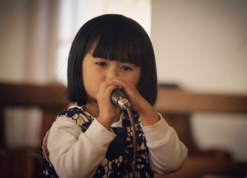 Close-up portrait of cute girl holding camera at home