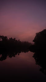 Silhouette trees by lake against romantic sky at sunset